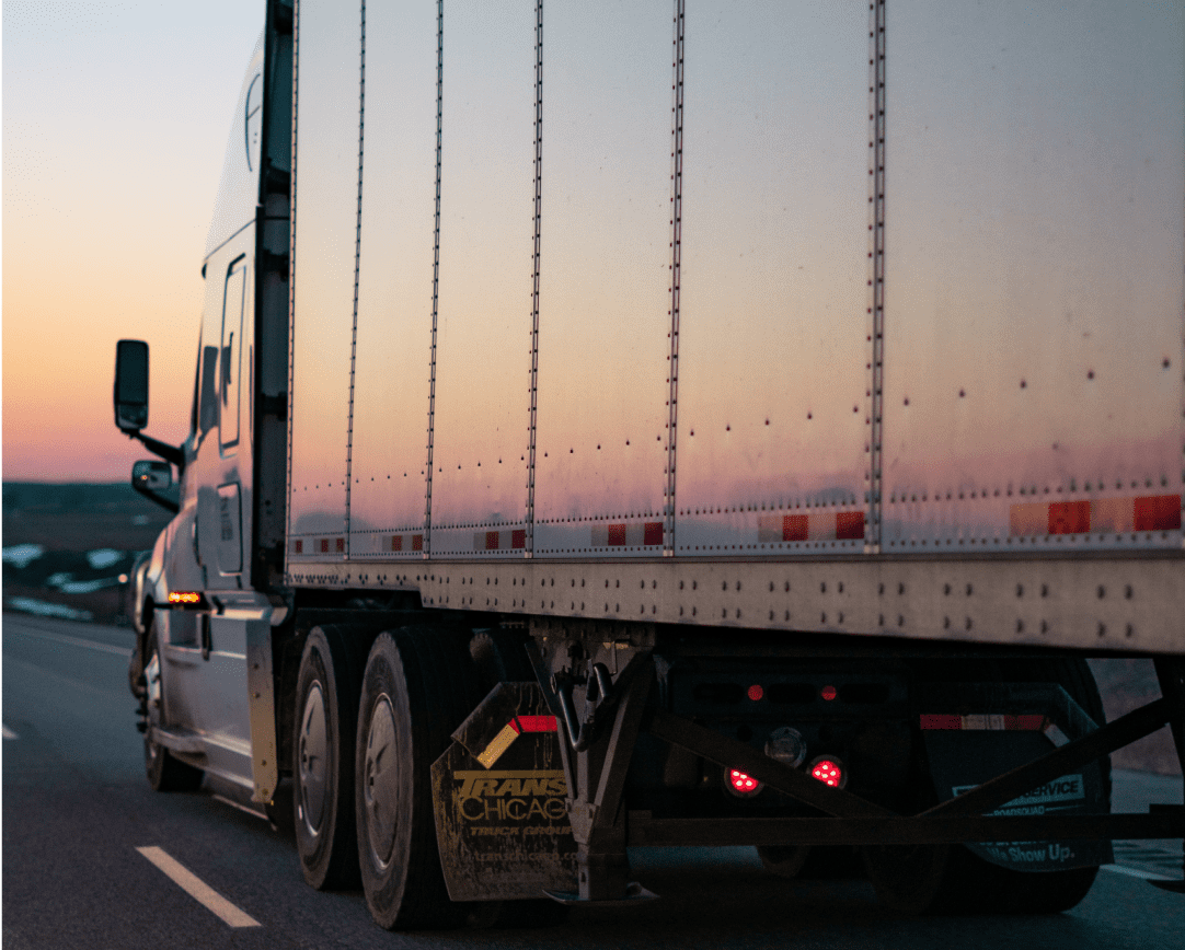 Truck with trailer driving down road during sunset